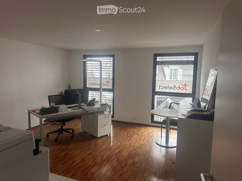 An office with a desk, two chairs, a printer, a computer, and a window.
