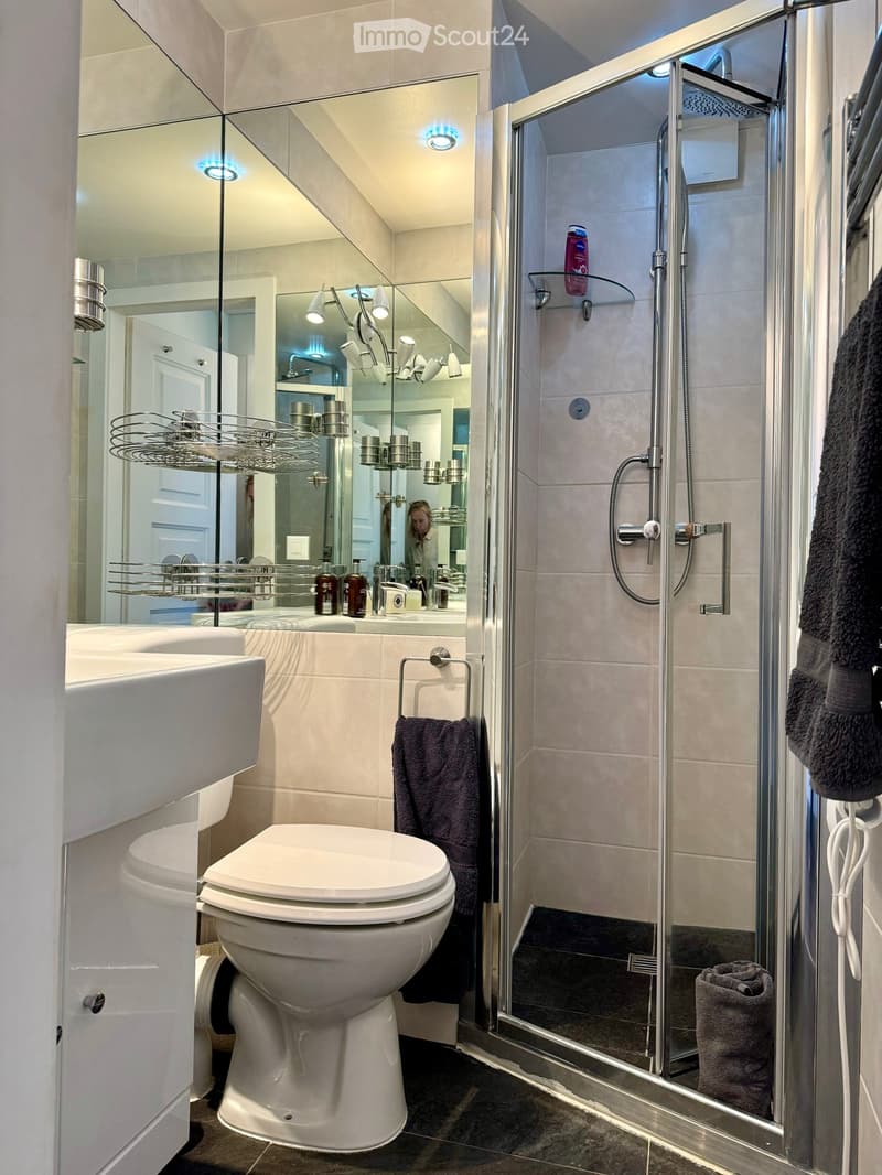modern bathroom with white toilet, white sink, glass shower enclosure, mirror, towel rack, and towel