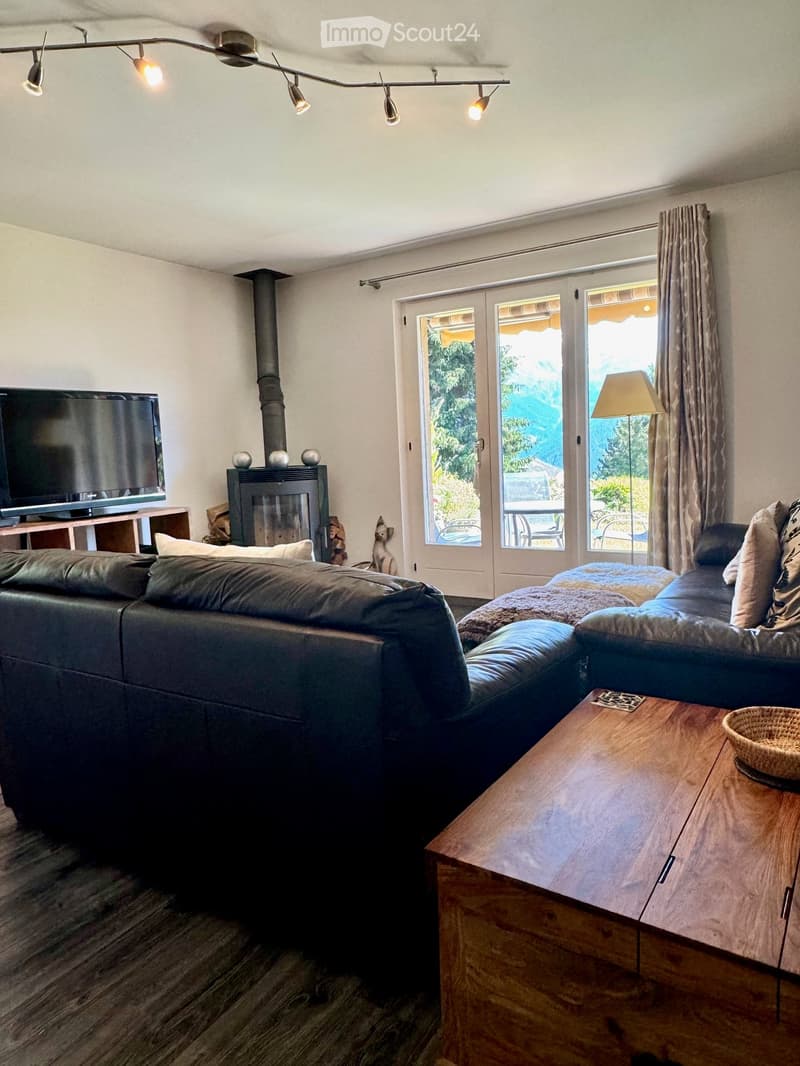 Living room with black leather sofas, wooden coffee table, fireplace, flat screen TV, sliding glass doors, wooden flooring, ceiling lights, and a view of the outdoors.