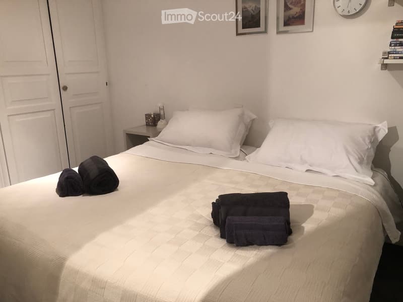 A bedroom with a bed, two nightstands, a clock, and two picture frames on the wall.
