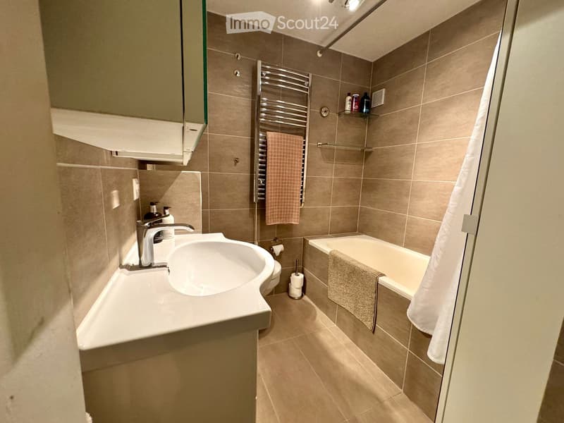 Bathroom with white sink, bathtub, toilet, towel rack, and tiled walls