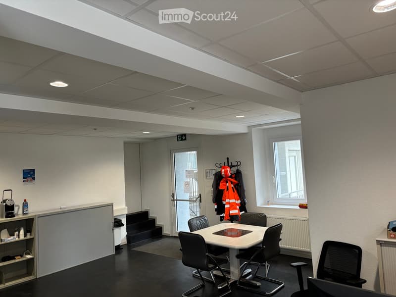 Office space with a round table, chairs, coffee machine, coat rack, and shelves.