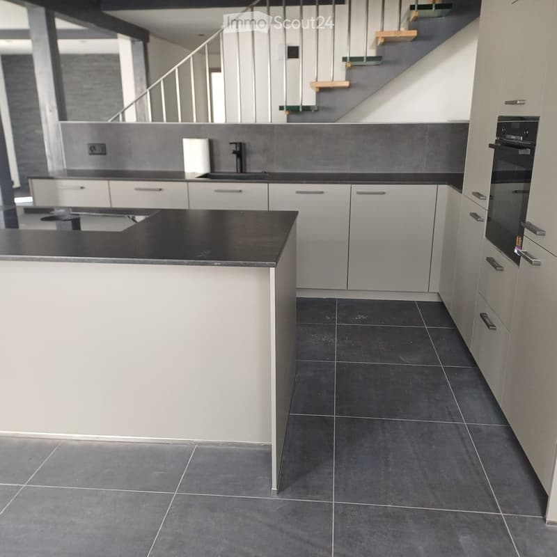 modern kitchen, white cabinets, black countertops, stainless steel sink, black tiled floor, built-in oven, open staircase