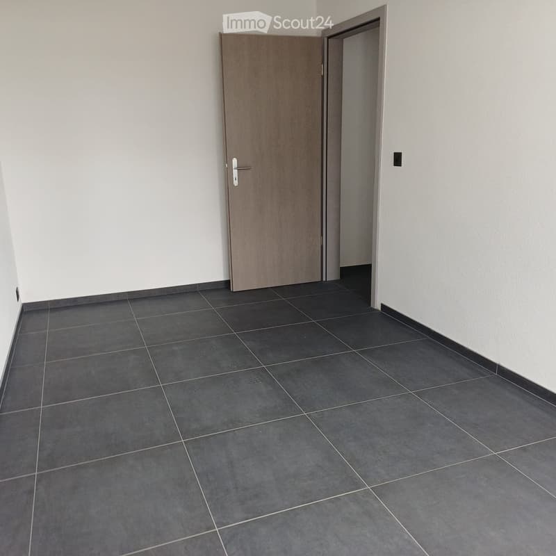 Empty room with gray tiles, white walls, wooden door, and an open door leading to another room