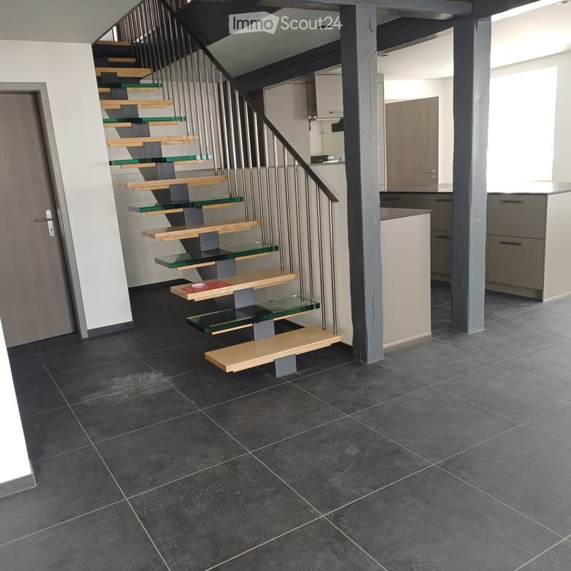 modern staircase with glass steps, gray tiled floor, white walls, gray door, kitchen area with cabinets