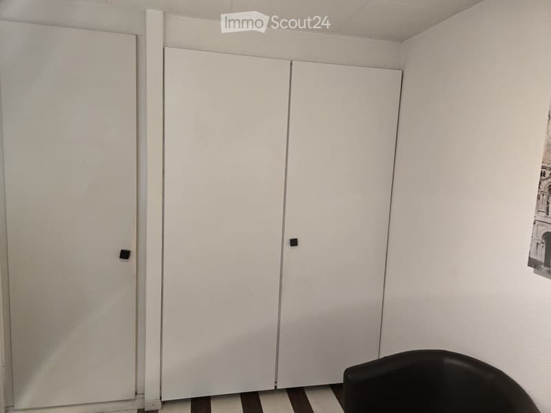 Two white sliding doors, black handles, white walls, black chair, white floor