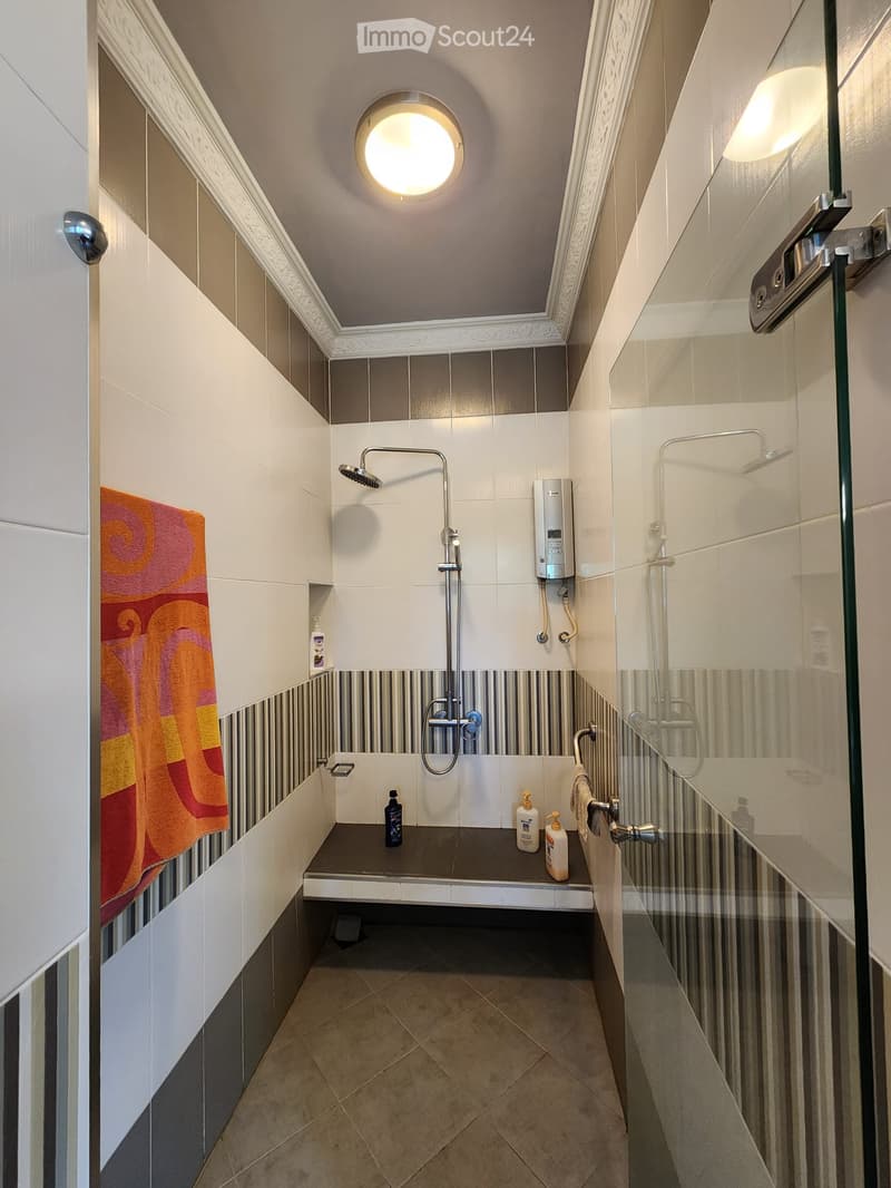 modern bathroom with shower, sink, and toilet, tiled walls, towel hanging, toiletries on the shelf