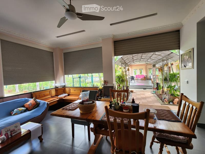 Dining area with wooden table, chairs, and a couch with pillows. A ceiling fan and picture frame are also present.