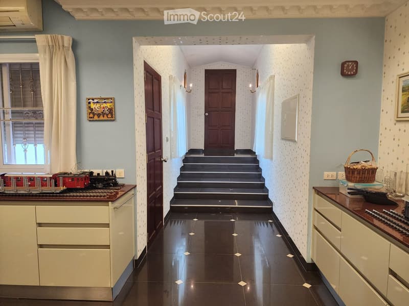 A hallway with a staircase leading to the upper floor, wooden doors, tiled floor, and a window with a curtain.