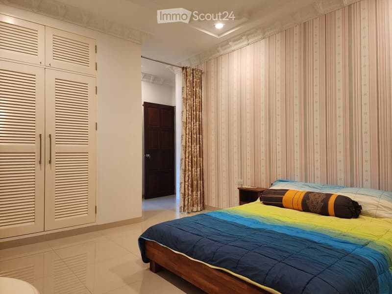 Bedroom with wooden bed, colorful bedspread, wooden nightstand, large wardrobe, striped wallpaper, wooden door, tiled floor.