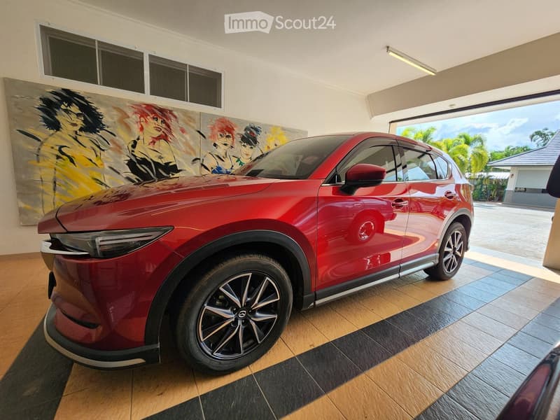 Red car parked in a garage with a tiled floor and a large painting on the wall