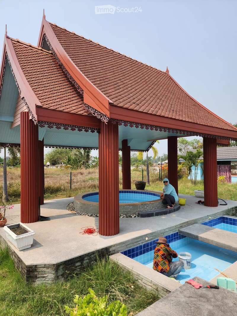 Pavilion with red roof, small swimming pool, large swimming pool, people cleaning pool, green grass, plants, trees