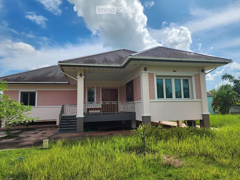 2 story house, pink and white exterior, brown roof, raised ground floor, balcony, front porch, large windows, surrounded by grass
