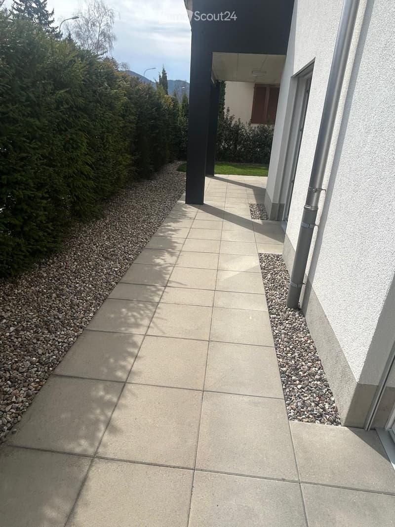 tiled walkway, gravel path, hedges, white wall, metal pipe