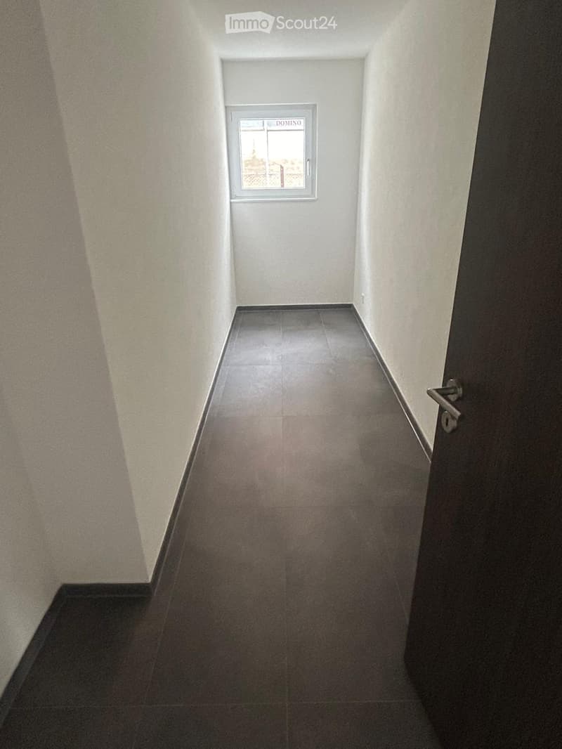 Empty hallway with white walls, dark tiles, small window