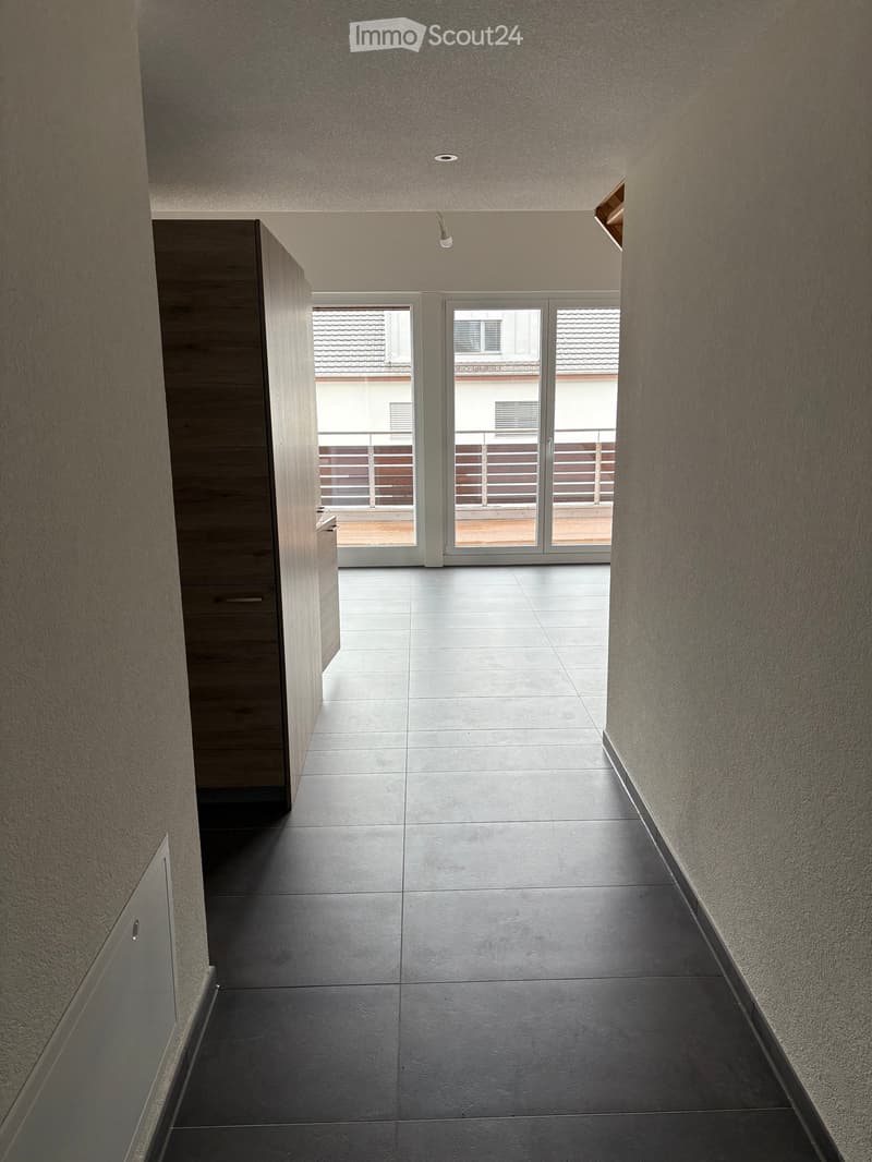 Empty hallway with tiled floor, wooden cabinet, sliding glass doors leading to balcony