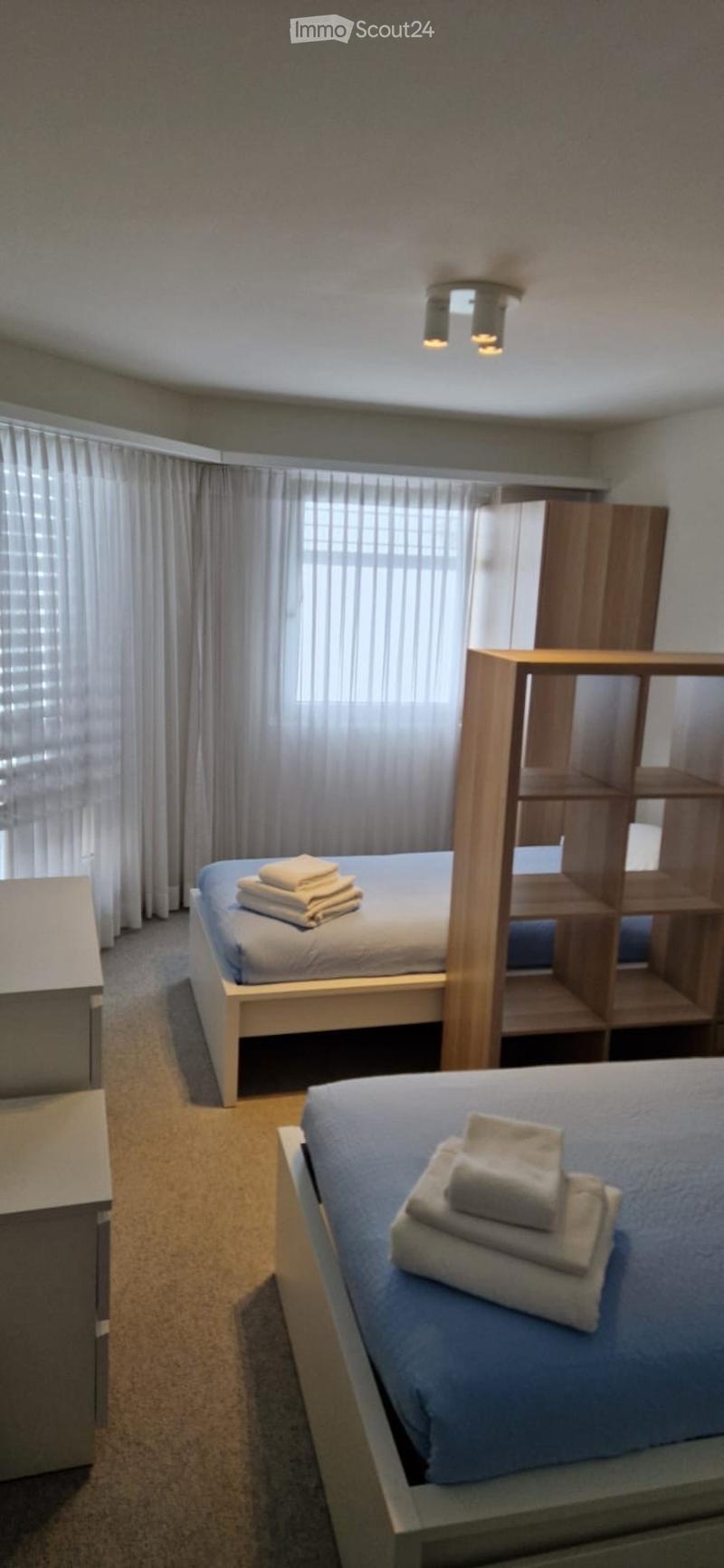 Two beds, white linens, white towels, white nightstands, white curtains, wooden shelves, wooden closets