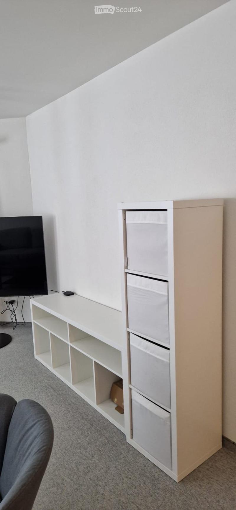 Living room with white shelves, TV, and a chair.