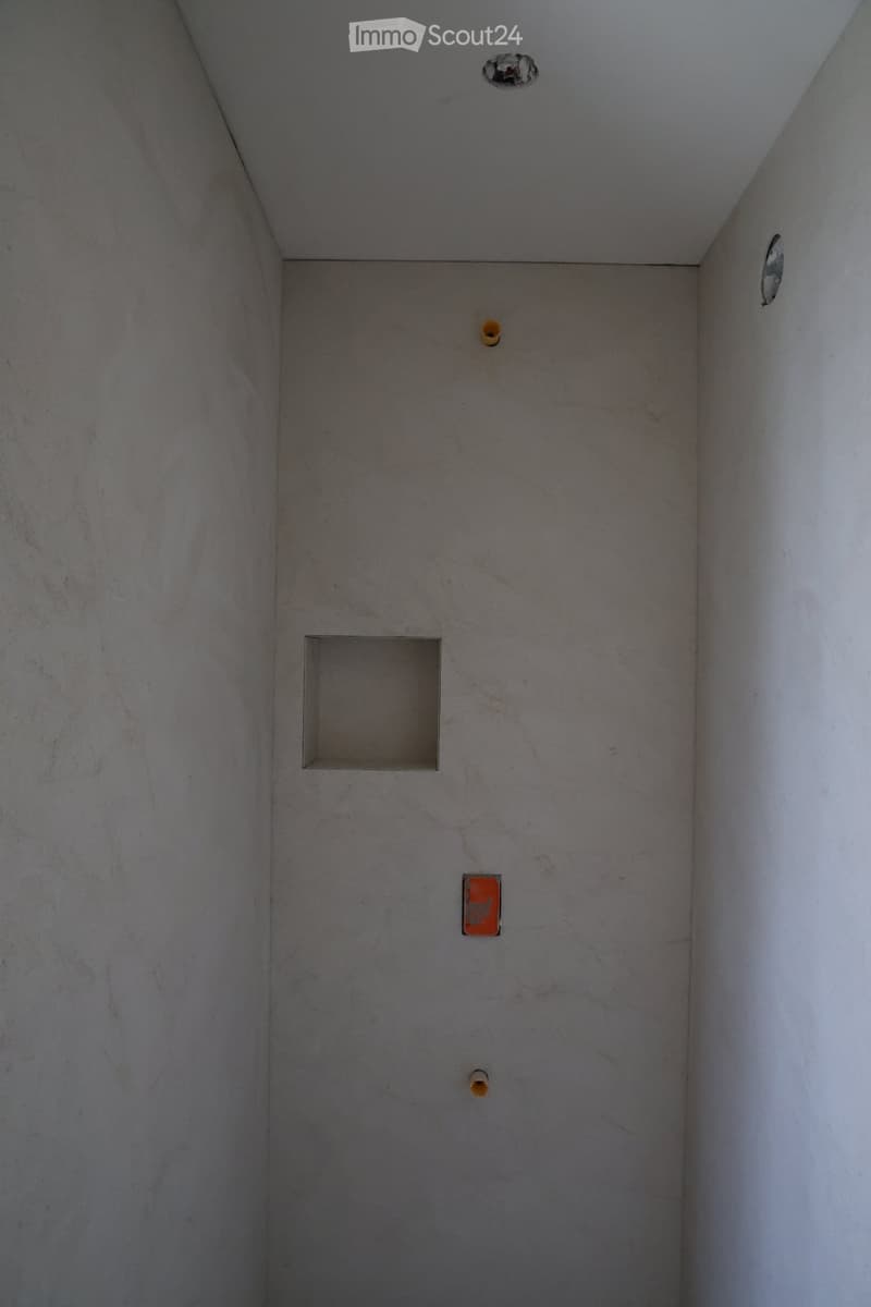 Empty room with bare concrete walls and ceiling, showing several unfinished spots and holes.