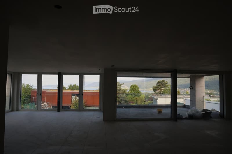 Empty room with large windows and a view of the landscape, featuring a tiled floor and exposed concrete ceiling.