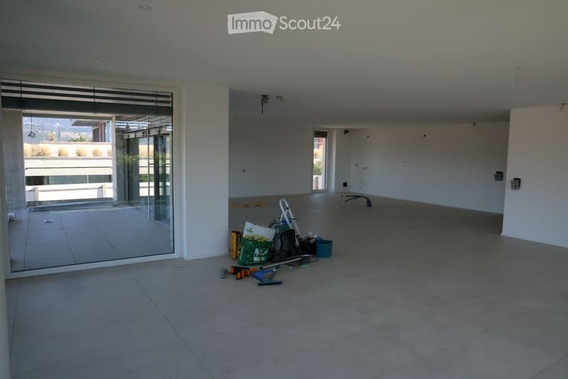 Empty room with tiled floor, white walls, large glass sliding doors leading to a balcony, and some construction materials and tools scattered on the floor.