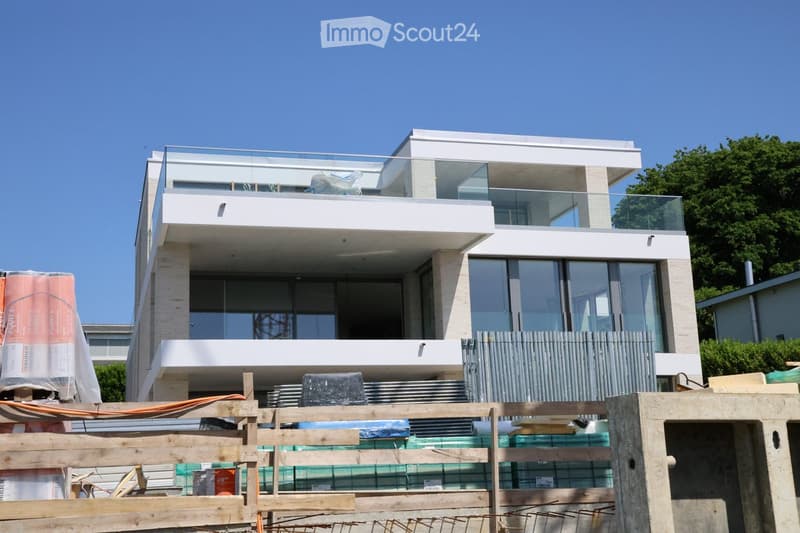 Modern two-story house with large glass windows and balconies, under construction with scaffolding and materials visible.