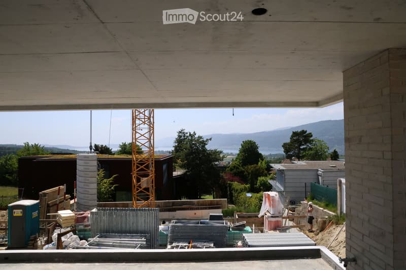 View from a raised ground floor showing construction materials, a crane, and a scenic view of mountains and water in the background.