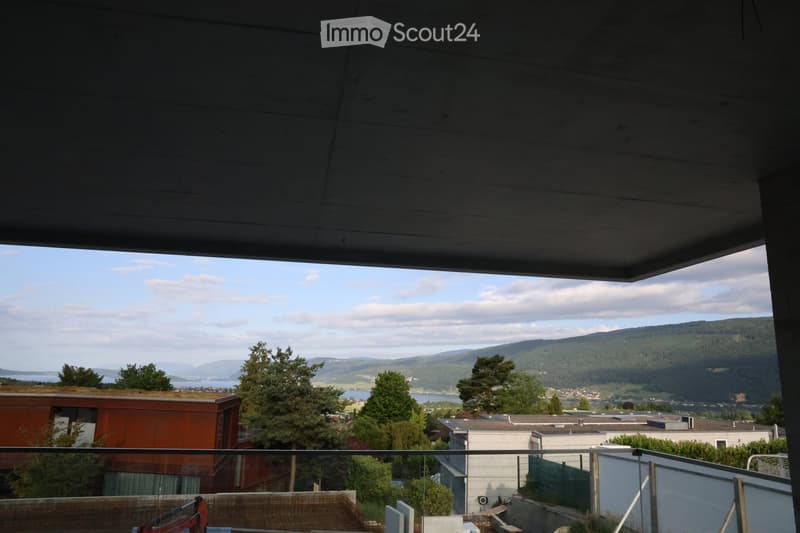 Balcony with a view of a cityscape, mountains, and a body of water, surrounded by trees and buildings.