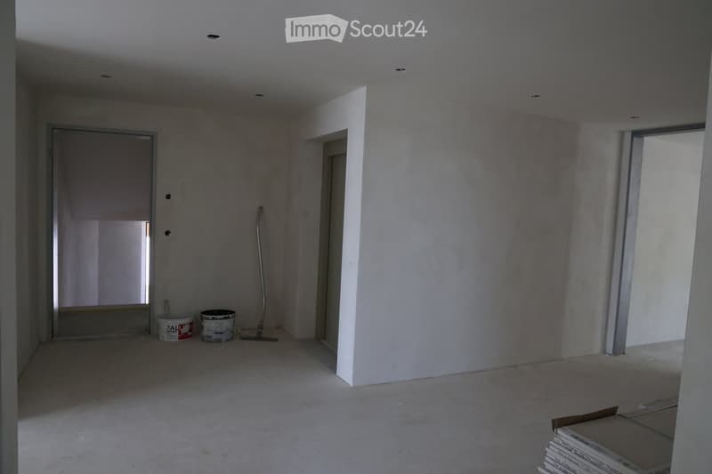 Empty room with bare walls and concrete floor, showing construction materials and tools near the doorway.