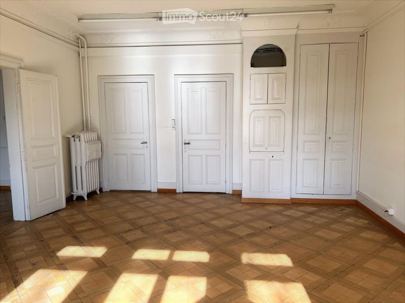Empty room with wooden parquet floor, white walls, white doors, and a radiator
