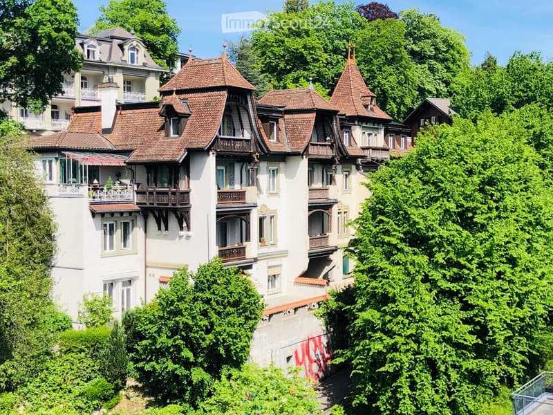 multi-story building, brown roof, white walls, balconies, surrounded by trees