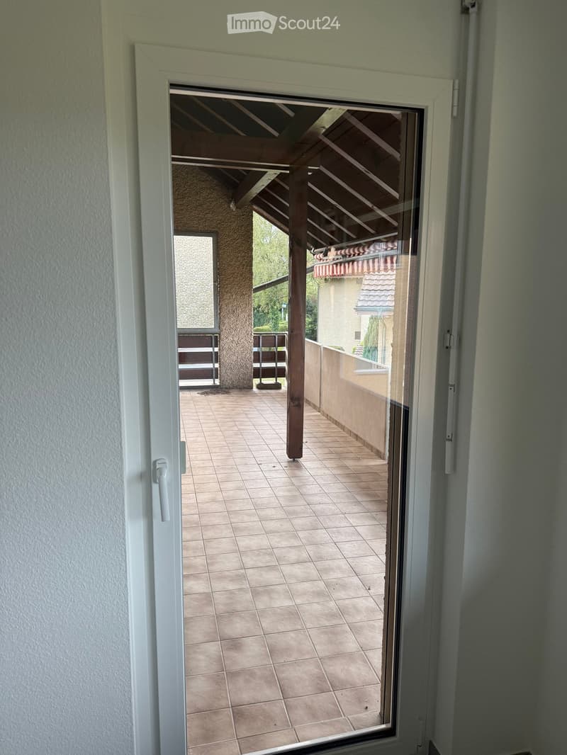 Open sliding door leading to a balcony with tiled floor and wooden ceiling