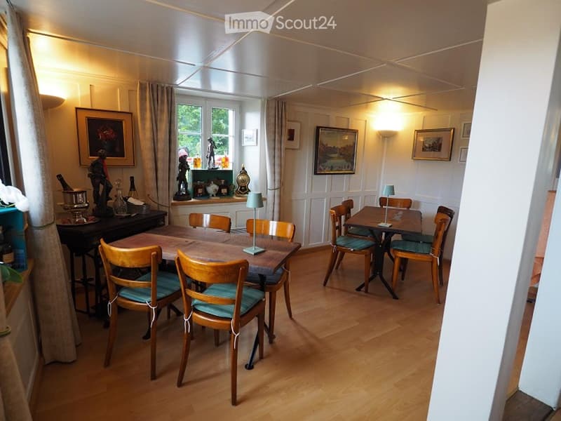 Dining room with wooden table and chairs, white walls, wooden floor, lamps, and picture frames