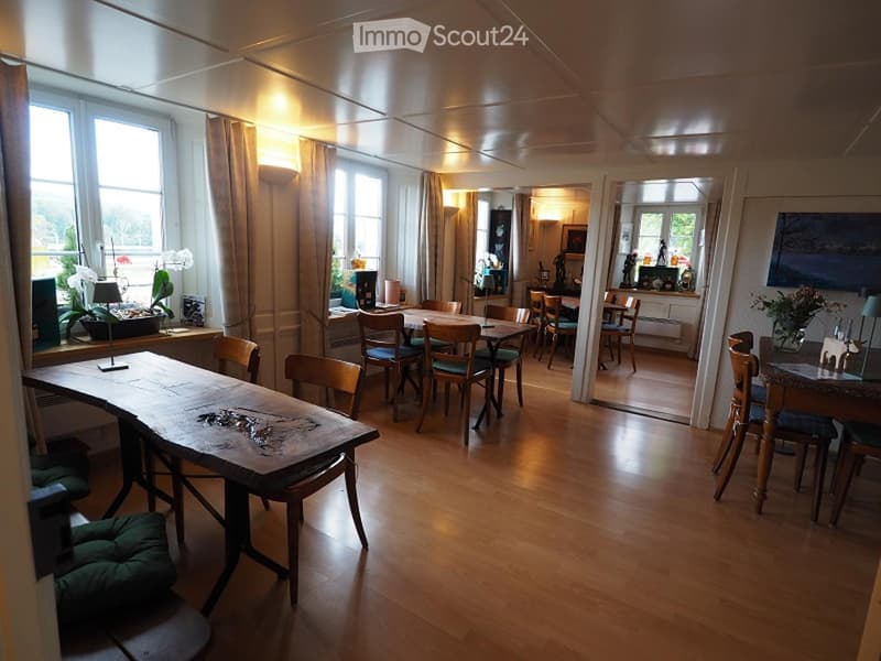 Dining room with wooden floor, large windows, dining tables, chairs, and decorative items