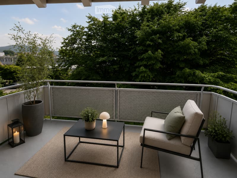 A modern balcony with a comfortable chair, small table, lamp, candle, and potted plants, overlooking a lush green area.