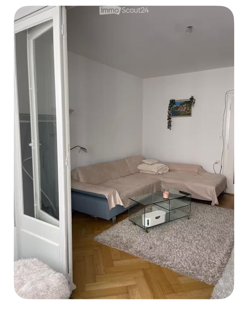 A living room with a couch, a glass table, a rug, and a lamp.