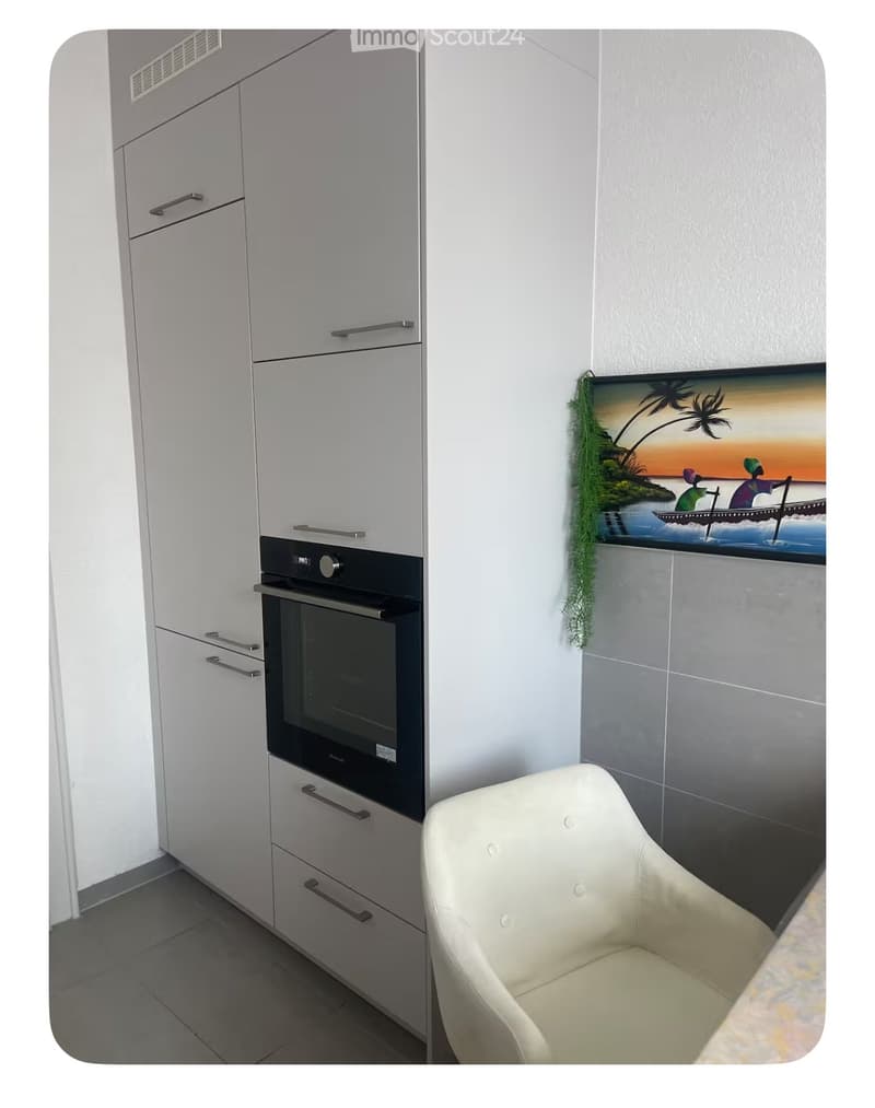 modern kitchen with white cabinets, black oven, white chair, tiled floor, painting on wall