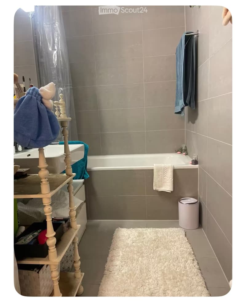 Bathroom with bathtub, shower curtain, towels, rug, trash bin, shelves with storage boxes, and a sink.
