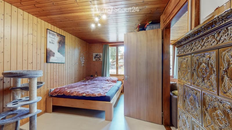 bedroom with wooden walls, bed, cat tree, wooden door, window with curtains, decorative items