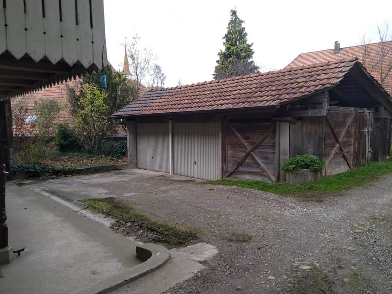Garage with two doors, red roof, concrete driveway, wooden structure, plants