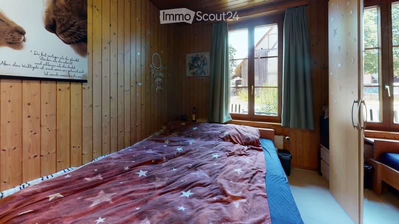 bedroom with bed, wooden walls, window with curtains, picture on the wall, trash bin, small desk
