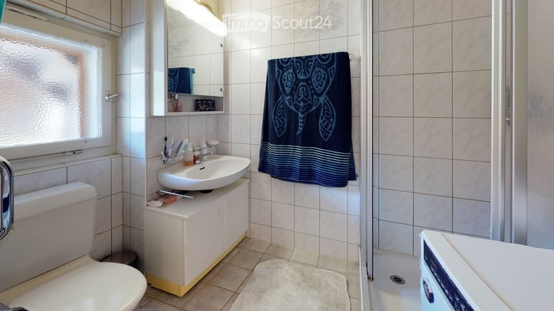 white tiled walls, white toilet, white sink, white shower, blue towels, white rug, white cabinet, white washing machine