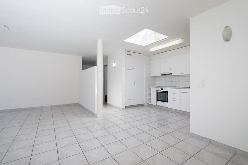 Empty kitchen with white tiled floor, white cabinets, and built-in appliances including an oven. The space features a skylight and recessed lighting.
