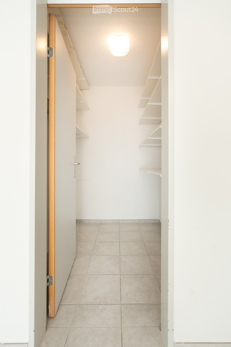 Empty room with beige tiled floor, white walls, built-in shelving unit, and a round ceiling light fixture.