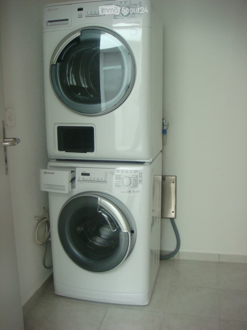Stacked white washing machine and dryer, located in a corner of a room