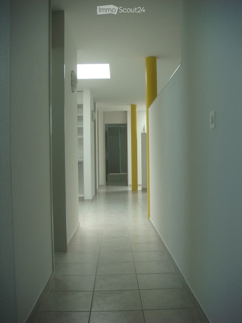 Empty hallway with white walls, yellow pillars, tiled floor, and a skylight