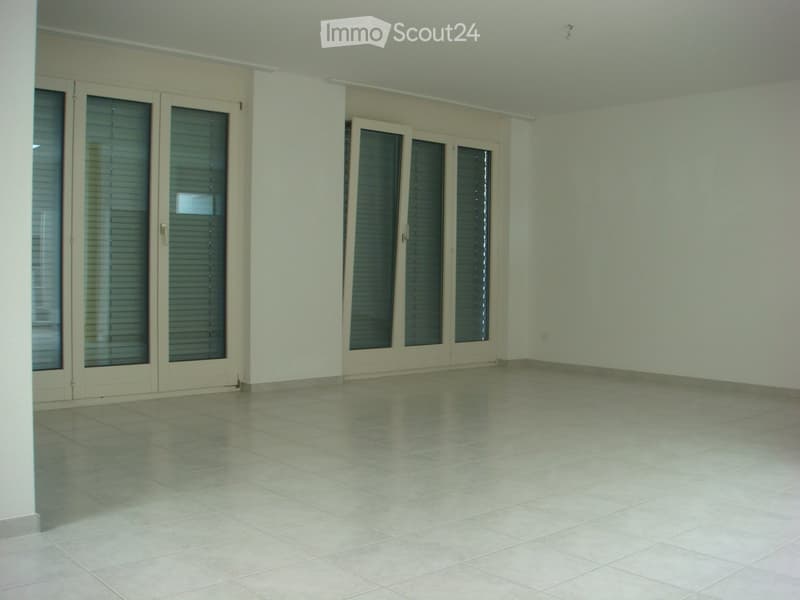 Empty room with white walls, white tile flooring, three large glass doors with blinds