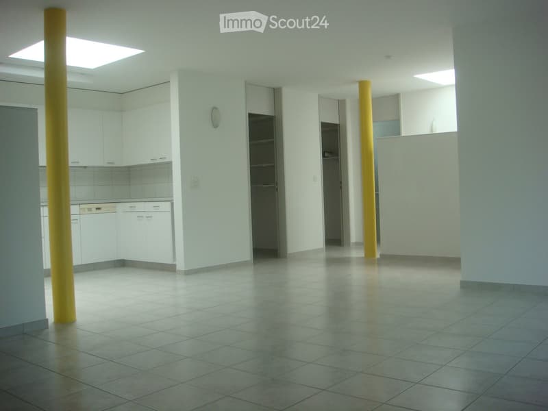 Empty room with white walls, tiled floor, two yellow pillars, kitchen area with cabinets and appliances, two closets, and two skylights.
