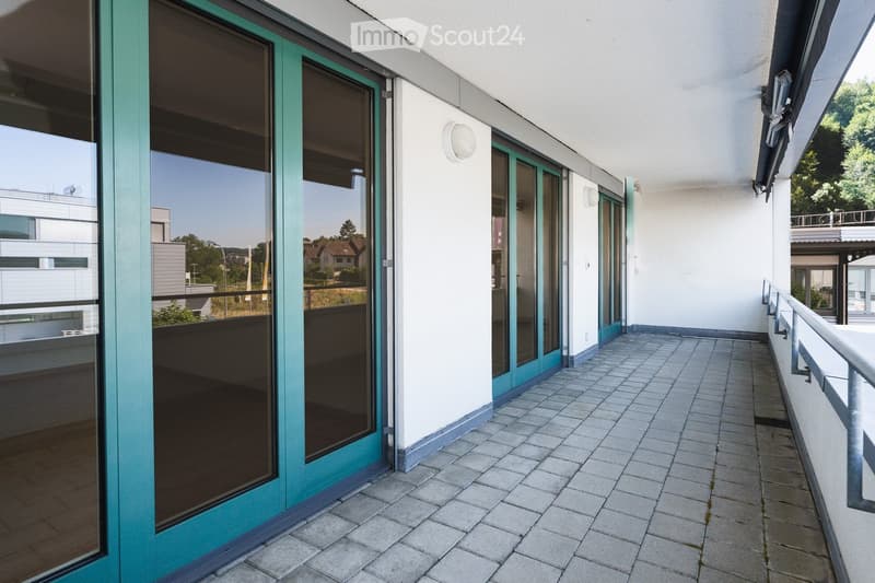Balcony with tiled floor, glass doors, metal railing, and a view of surrounding buildings and greenery.