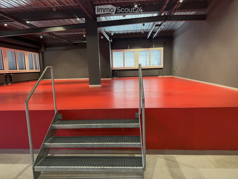 Empty room with red floor, metal stairs, metal handrails, windows, gray walls